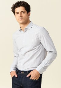 Lange mouwen overhemd met knoopsluiting in lichtgrijs met kleine blauwe patronen, voorzien van een kraag en manchetten met één knoop, gecombineerd met donkere spijkerbroek.