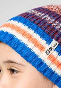 Bonnet en tricot avec des rayures rouges, bleues, orange et blanches. Inclut une étiquette sur le côté. Texture douce, forme arrondie.