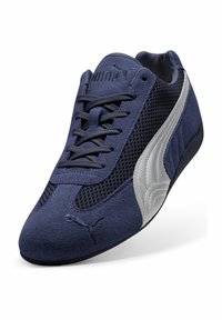 Mornarsko plava sportska cipela s gornjim dijelom od antilopa i mrežice, sustavom vezanja, srebrnim detaljima i gumenim potplatom. Ima logo na jeziku i sa strane.