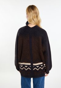 Maglione marrone scuro dalla vestibilità ampia, caratterizzato da motivi geometrici in beige e blu scuro lungo l'orlo e le spalle. Morbida texture in lana.