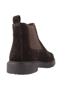 Stivale Chelsea in suede marrone scuro con pannello elastico laterale, linguetta sul tallone e suola in gomma spessa, visto da un angolo posteriore.
