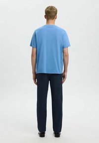 Gai zils īsroku krekls ar brīvu piegriezumu, apvienots ar tumši zilām taisnām biksēm. Vienkārša, gluda tekstūra un apaļa kakla izgriezums.