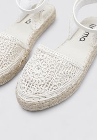 Zapatos de espadrilles blancos con parte superior de tela tejida decorativa, plantilla trenzada de yute y tacón plano. Correa de tobillo ajustable para un ajuste seguro.