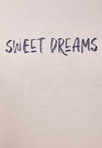 Beige cotton t-shirt featuring the phrase "SWEET DREAMS" in dark blue brushstroke font. The fabric has a smooth texture.