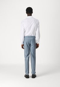 Chemise blanche à manches longues et pantalon bleu clair, avec une coupe ajustée et des chaussures noires contrastantes, vues de dos.