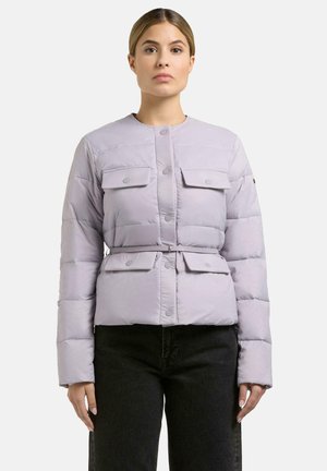 Kobieta ubrana w jasnofioletową pikowaną kurtkę z zatrzaskami, kieszeniami z klapkami i paskiem w talii, w połączeniu z czarnymi spodniami, na białym tle.