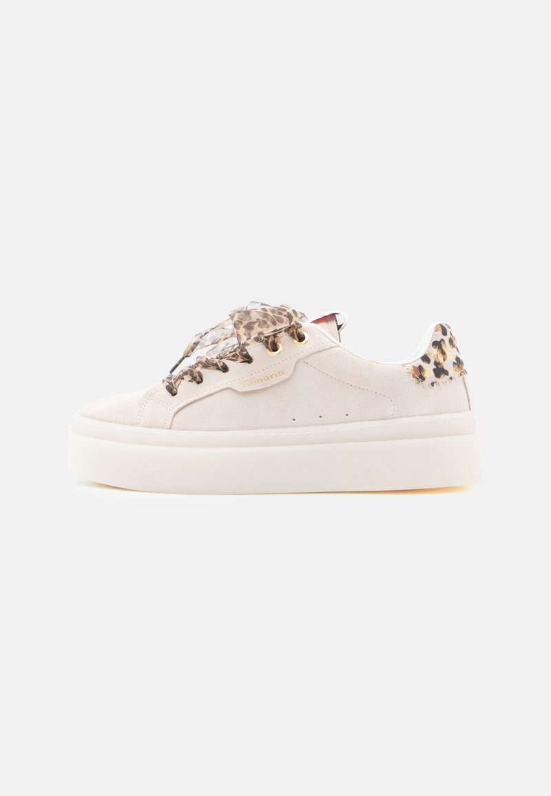 Ανοιχτό μπεζ σουέτ αθλητικό παπούτσι με χοντρή λευκή σόλα, διακοσμημένο με κορδόνια και λεπτομέρειες σε σχέδιο ζώου στη φτέρνα. Διακρίνεται από μινιμαλιστική σχεδίαση.