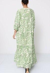 Robe maxi en vert clair avec un imprimé botanique blanc. Manches longues, niveaux froncés et tissu légèrement texturé. Design mi-mollet.