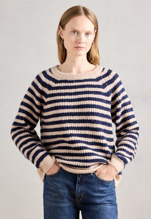 Stripet genser i krem og marineblå, med ribbestrikket halsringning og mansjetter, avslappet passform og strukturert strikkemønster. Kombinert med denim.