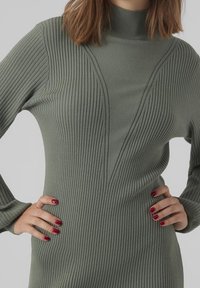 Robe col roulé en maille côtelée vert mute avec des lignes verticales, coupe ajustée et motif en forme de V sur la poitrine.