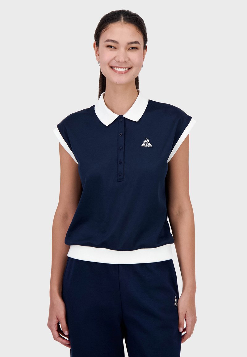 Polo de color azul marino con un cuello y puños blancos, que cuenta con una tapeta de botones en la parte delantera y un detalle de logo en el lado izquierdo del pecho. Acabado en tejido suave.