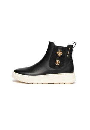 Zwarte leren enkelboot met witte zool, elastisch zijpaneel, trekband en gouden edelsteenversieringen aan de zijkant.
