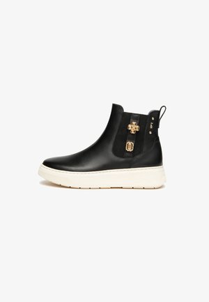 Bottine en cuir noir avec semelle blanche, panneau latéral élastique, tirette et embellissements en gemmes dorées sur le côté.