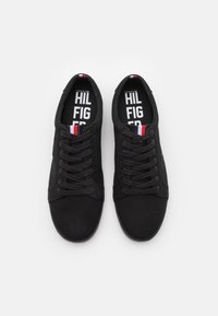 Svarta kanvas sneakers med runda tår, platta snören och märkesinlägg med en logotyp. Sidan har en diskret accent i röd, vit och blå.