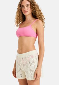 Cropped top rosa a costine con spalline sottili abbinato a pantaloni corti in maglia color crema con un motivo a treccia e una vita elastica.