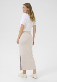 Vaalean beige, vartalonmyötäinen maxi-hame, jossa on korkea halkio. Se on yhdistetty valkoiseen lyhythihaiseen t-paitaan ja beigeihin tennareihin. Suuri kangas on sileä.