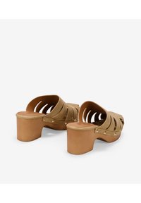 Sandalias de plataforma de ante marrón con diseño de punta abierta, que presentan detalles cortados y acentos metálicos alrededor de la base.