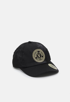 Casquette de baseball noire avec logo circulaire doré Versace Jeans Couture sur le devant et autocollant assorti sur la visière, présentée sur fond blanc.