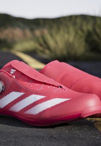 Różowe buty sportowe z gładką, syntetyczną cholewką, białym wzorem w trzy paski, zabezpieczającym mechanizmem zapięcia oraz teksturowaną podeszwą.