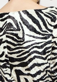 Tissu en velours noir et blanc avec un motif rayé zebré, présentant une texture brillante et une apparence lisse et douce.