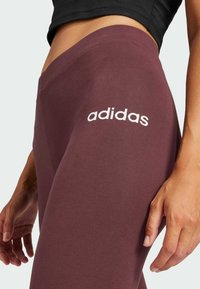 Bordo tajice izrađene od mekane tkanine, s bijelim "adidas" logotipom na lijevom bedru. Prilagođen dizajn s glatkom teksturom.