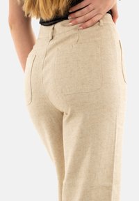Pantaloni beige a vita alta con tessuto testurizzato. Presentano due tasche posteriori e una silhouette su misura, adatti per un abbigliamento casual o formale.