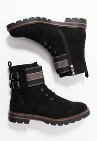 Stivaletti alla caviglia in suede nero con una fascia elastica a contrasto e doppia fibbia, dotati di una suola testurizzata e una cerniera laterale per un facile indossamento.