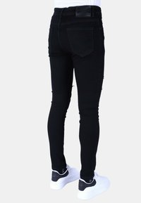 Zwarte skinny jeans met een gladde textuur, versleten accenten en een hoge taille. Gecombineerd met witte sneakers met zwarte hielaccenten.