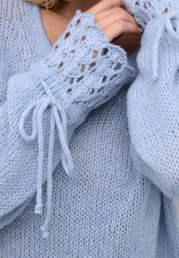 Ljusblå stickad tröja med lös passform, intrikat spetsdetaljering på ärmarna och bandknytningar vid ärmsluten.