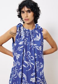 Blaues ärmelloses Kleid aus leichtem Stoff, mit einem weißen Blumenmuster, gerafftem Ausschnitt und Schulterbindebändern.