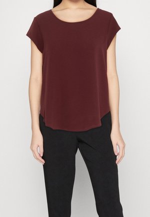 Haut bordeaux à manches courtes avec un col rond, en tissu doux, et un ourlet asymétrique, accompagné de pantalons noirs. Détails texturés minimaux.