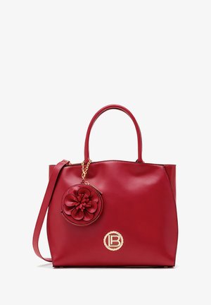 Red leather tote bag with a textured finish, features a circular floral charm, gold hardware, and a logo accent on the front.