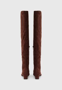 Bottes en suède marron jusqu'au genou avec un design ajusté, détail de fermeture éclaire sur le côté, et un petit talon pour plus d'élévation. Texture lisse sur l'ensemble.