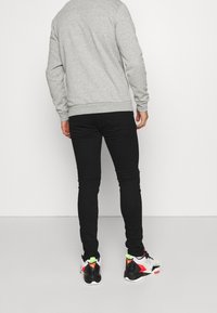 Sudadera gris claro, pantalones estrechos negros y zapatillas negras con acentos en rojo y verde neón. Textura suave con diseño ajustado.