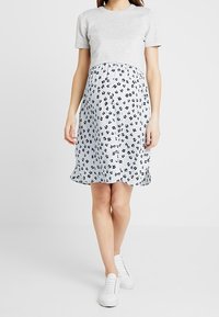 Un haut gris à manches courtes avec un col rond associé à une robe florale à motifs, arrivant aux genoux, en bleu et blanc, portée avec des baskets blanches.