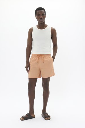 White ribbed tank top, peach swim shorts with drawstring, and brown slide sandals. Simple design, soft fabric, and relaxed fit.