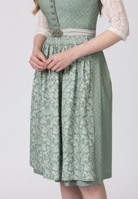 Grünes, gemustertes Kleid mit tailliertem Oberteil, Spitzeärmeln und einem gerafften Rock mit floralen Designs. Silberne Gürtelschnalle als Detail an der Taille.