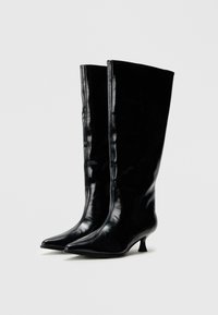 Čierne kožené čižmy po kolená s lesklým povrchom, špicatou špičkou a nízkym, zakriveným opätkom. Čižmy majú bezšvový dizajn.