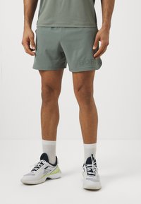 Pantalones cortos deportivos verdes hechos de tela ligera, con el texto "BORG" en un tono más oscuro, combinados con zapatillas blancas y calcetines hasta la altura del tobillo.