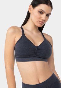 Bralette suave de color gris oscuro con diseño de escote en V, centro fruncido y tirantes ajustables. Fabricado con un material texturizado y elástico.