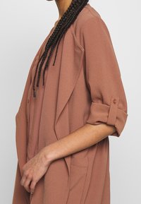 Lättviktig, texturerad, rosafärgad ytterjacka med öppen framdel, rullade ärmar och sidofickor.