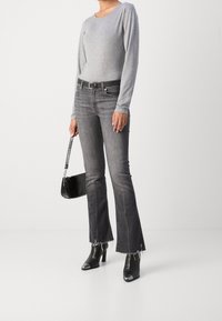Graues Langarmoberteil, dunkelgraue Schlagjeans mit ausgefranstem Saum, schwarze Stiefeletten mit Absatz und metallischen Akzenten sowie eine kleine schwarze Handtasche.