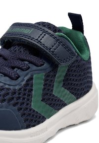 Marinblå nät sneaker med gröna accenter, utrustad med ett kardborreband och kontrasterande textyroverflöde. Vit sula med ett mönstrat grepp.