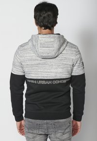 Pullover con cappuccio caratterizzato da blocchi di colore grigio e nero, tessuto testurizzato e testo stampato bianco sulla schiena. Polsini e orlo elasticizzati.