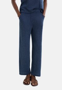 Granatowe spodnie z szerokimi nogawkami wykonane z teksturowanej tkaniny, z elastycznym pasem i bocznymi kieszeniami. Połączone z brązowymi klapkami.