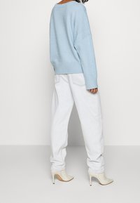 Jasnoniebieski, oversize sweter z miękkiego dzianiny, w połączeniu z luźnymi białymi dżinsami i beżowymi botkami na wysokim obcasie.