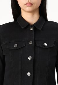 Svart denimjakke med klassisk krage, fem sølvfargede trykknapper og to brystlommer med klaffelukking. Glatt tekstur og tettsittende design.
