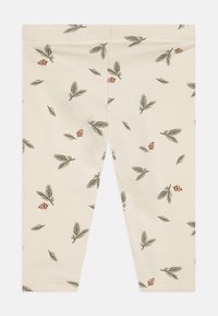 Beige leggings med et mønster av grønne blader og små brune furukongler. Laget av mykt, elastisk stoff. Tett passform med elastisk midje.