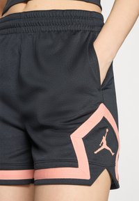 Shorts de sport noirs en tissu texturé avec des accents roses, dotés de poches latérales et d'un détail de logo sur l'ourlet inférieur.