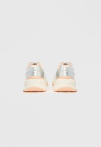 Silver sneakers with a smooth texture, featuring soft peach accents at the heel and tongue, and a cushioned, slightly elevated sole.